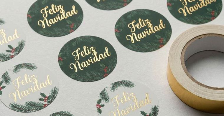 Etiquetas verdes redondas con Feliz Navidad en dorado y un rollo de cinta adhesiva