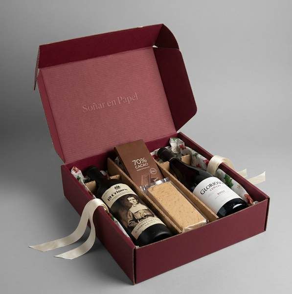Caja vino con tapa abierta que muestra botellas, turrón y chocolate con cinta marfil
