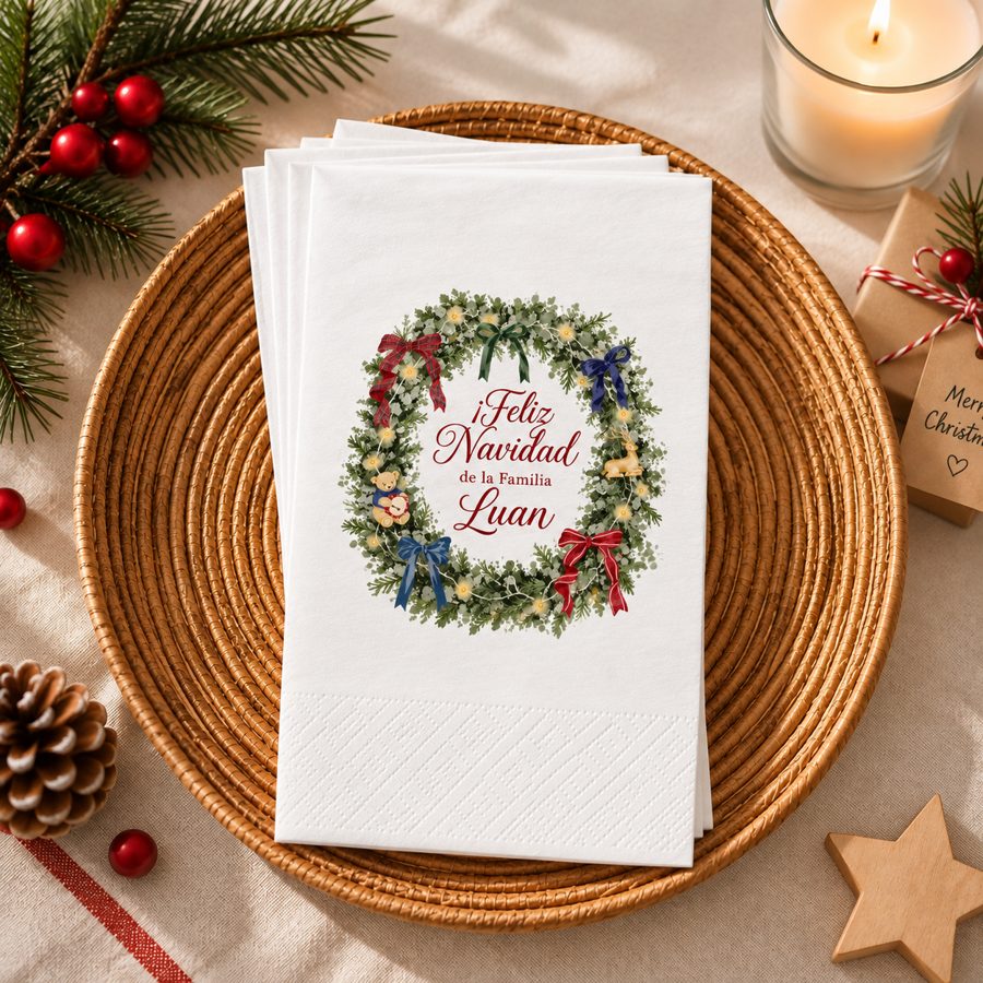 Servilletas hand towel blancas con corona navideña y mensaje personalizado de familia, sobre plato de mimbre